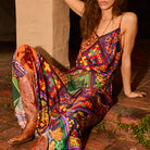 Woman seated on brick steps wearing a multicolour patchwork-print satin slip skirt with spaghetti straps and cowboy boots