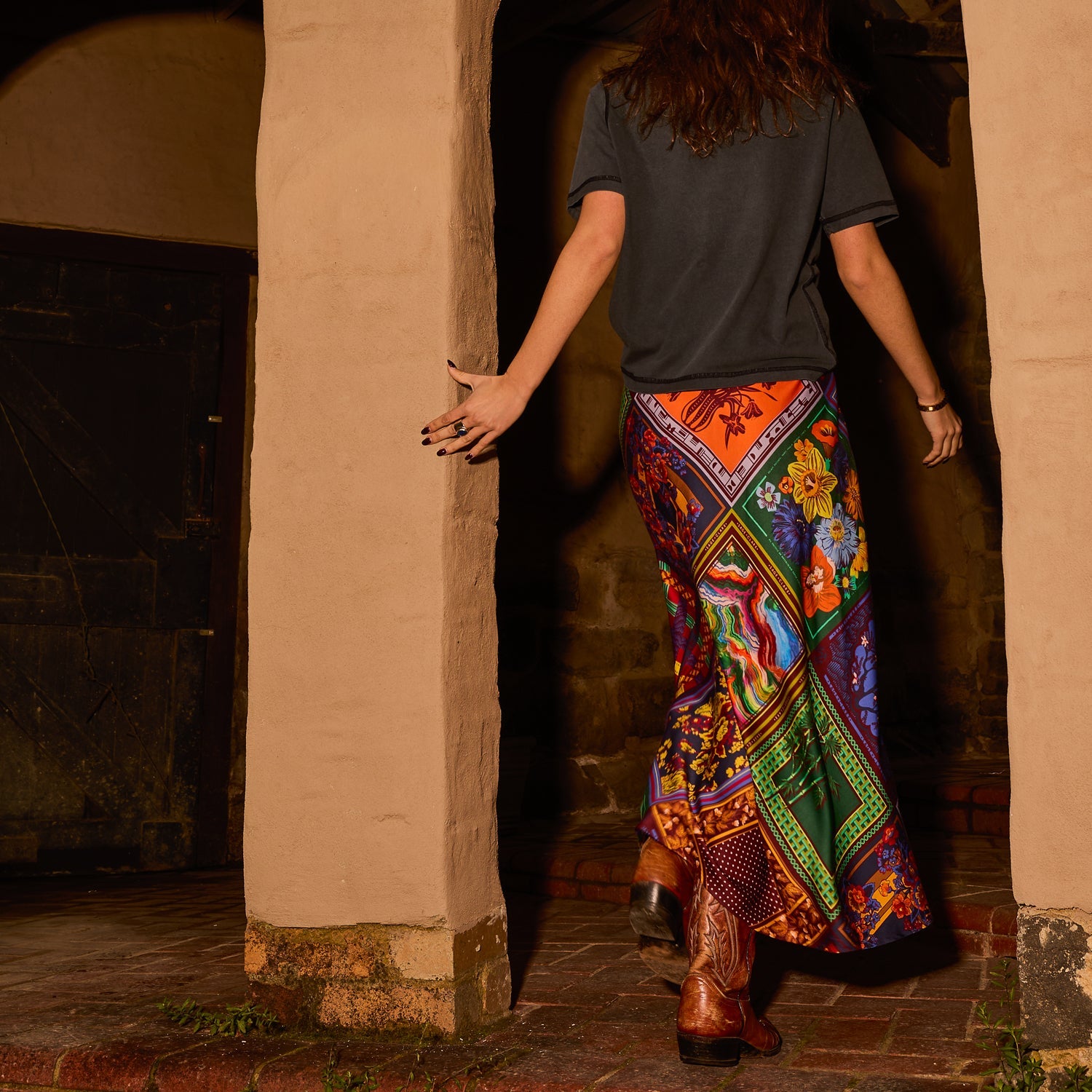 Back view of a multicolour patchwork-print satin maxi slip skirt styled with a grey tee and cowboy boots