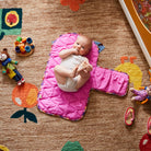 Stela Change Mat in bright pink quilted fabric with baby lying on padded surface surrounded by toys