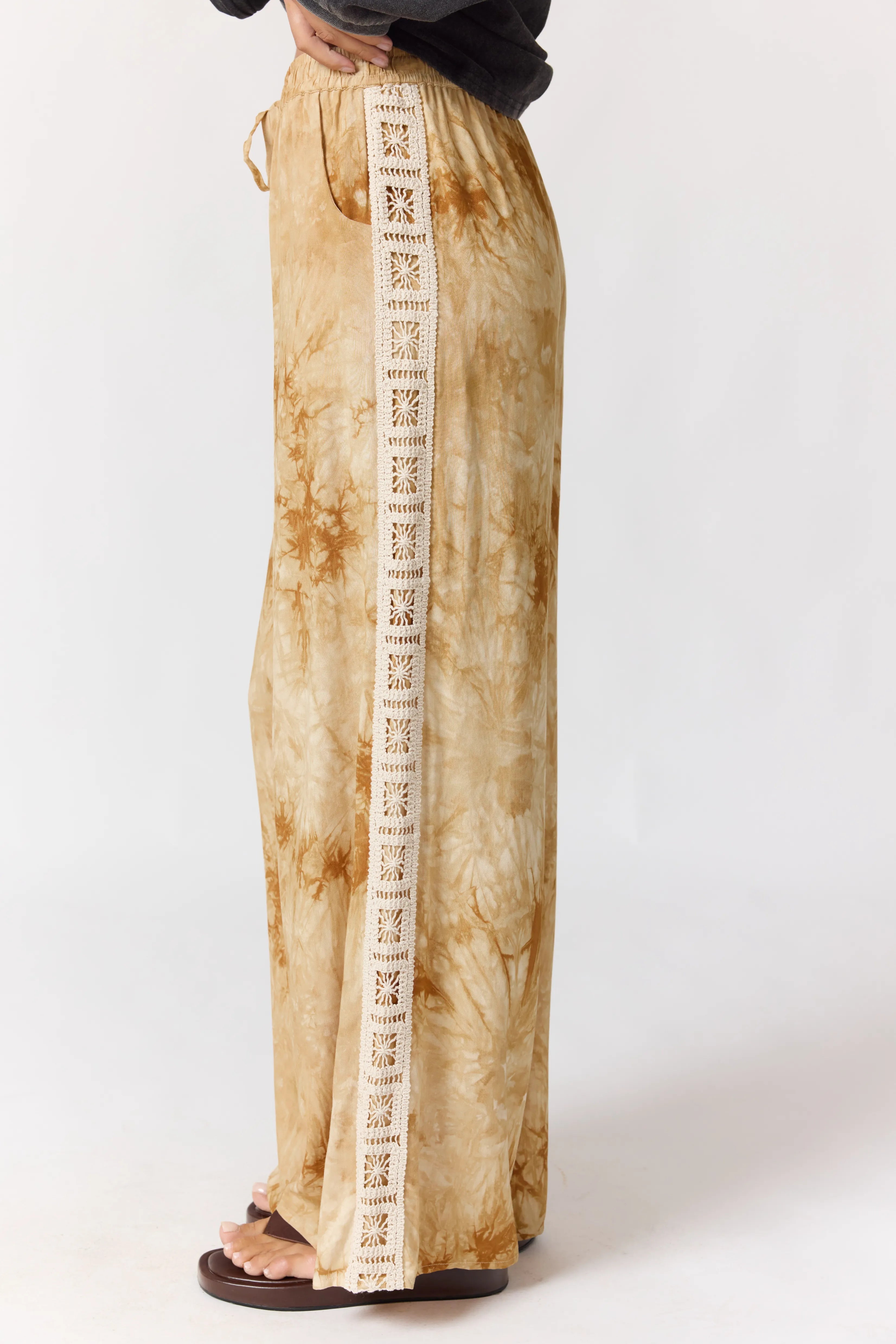 Seated view of Sunday Pants displaying crochet lace trim detail and tie-dye fabric pattern