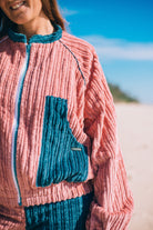 Close-up of pink corduroy surf bomber jacket showing teal contrast chest pocket ribbed texture and branded label