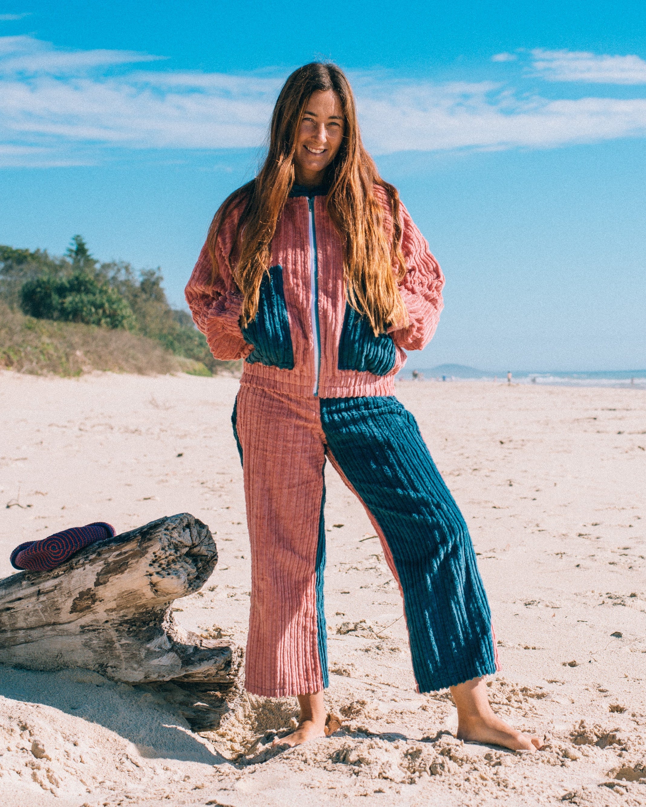 Full-length front view of pink and blue corduroy surf bomber jacket worn on the beach with zip-front and contrast pockets