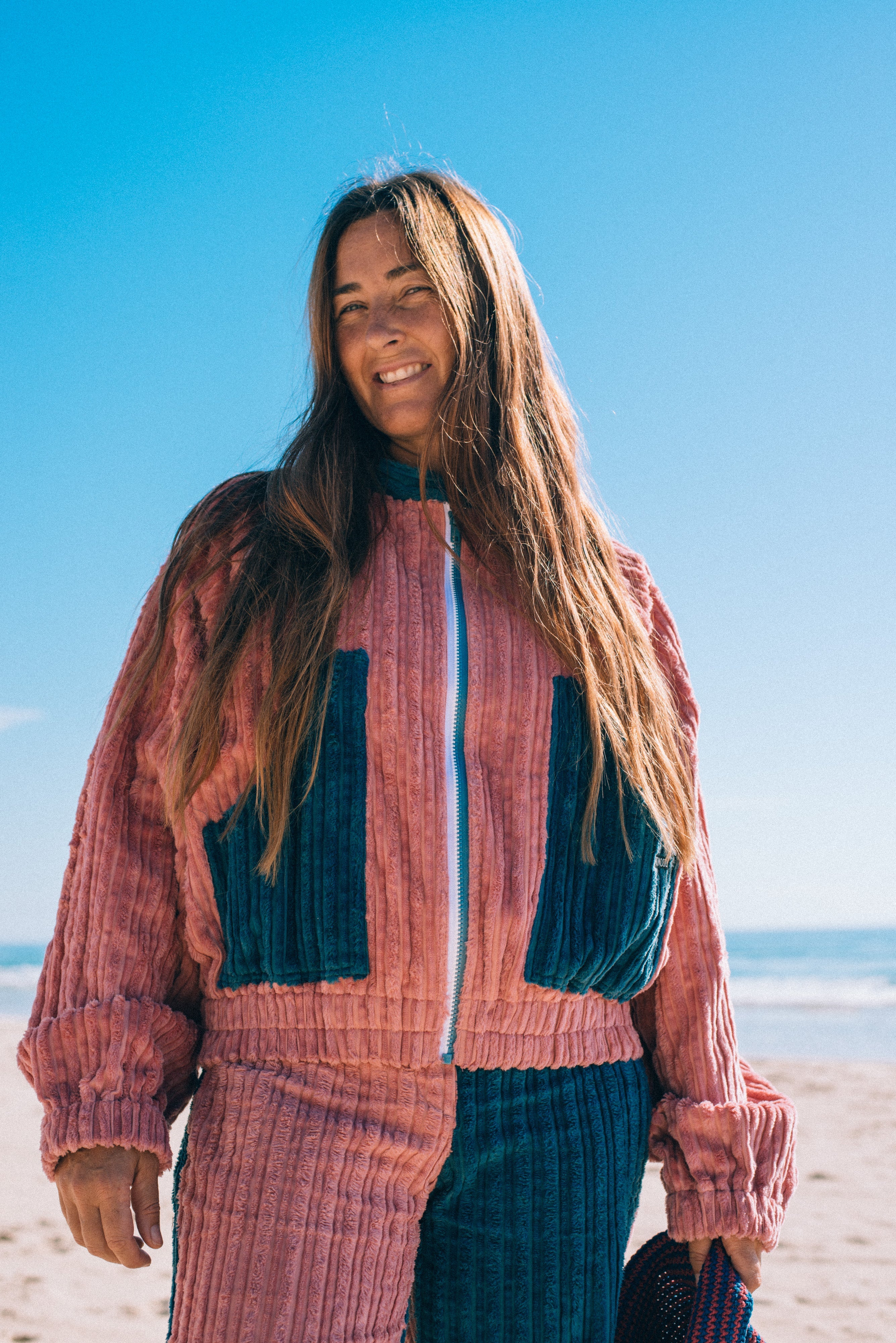 Front close-up of two tone pink and blue corduroy bomber jacket showing zip front teal collar and chest pockets at beach