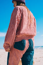Back view of pink corduroy surf bomber jacket showing ribbed texture elasticated hem and long sleeves at beach