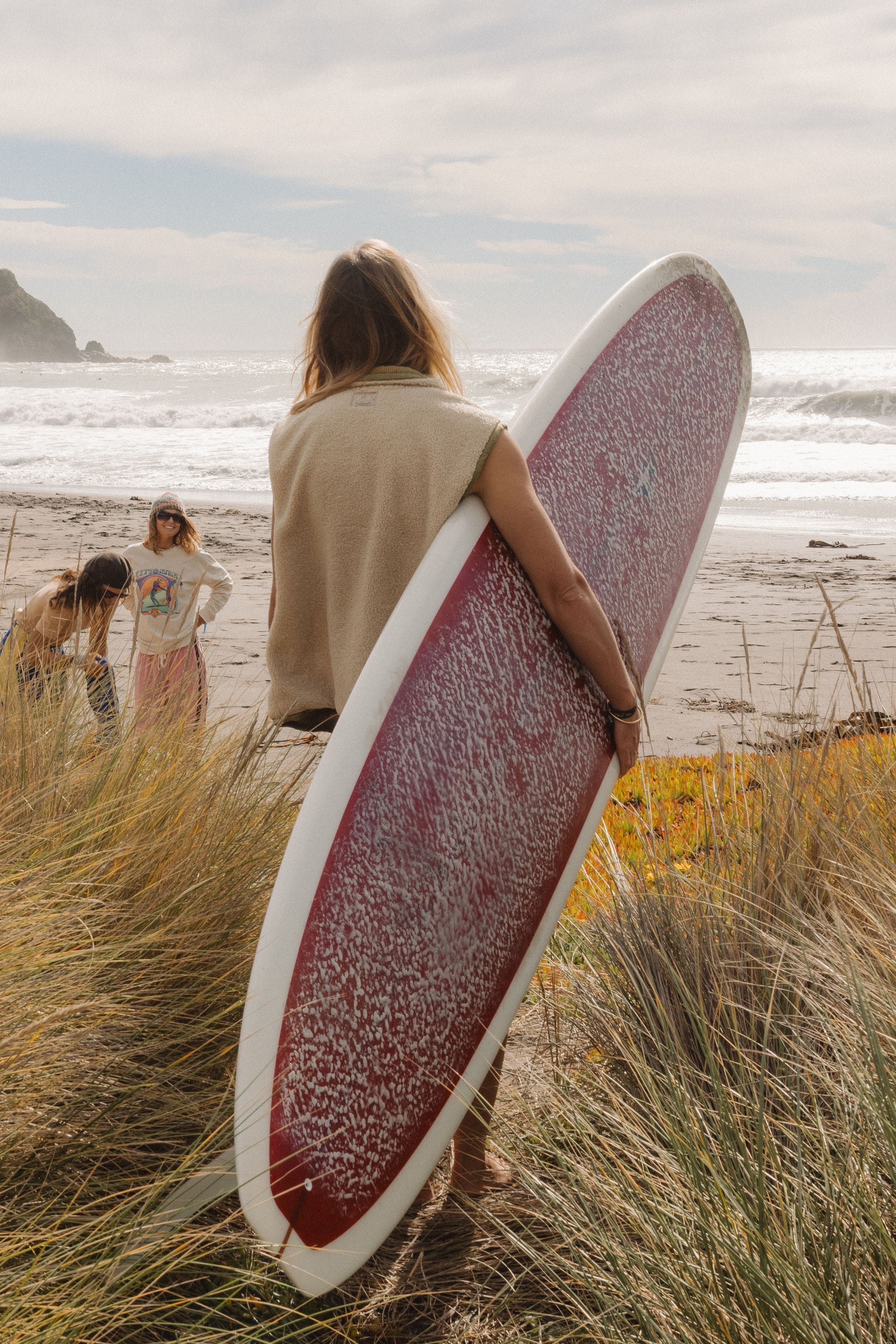Back view of the cream surf coach front zip vest in size M worn by a woman carrying a longboard at the beach