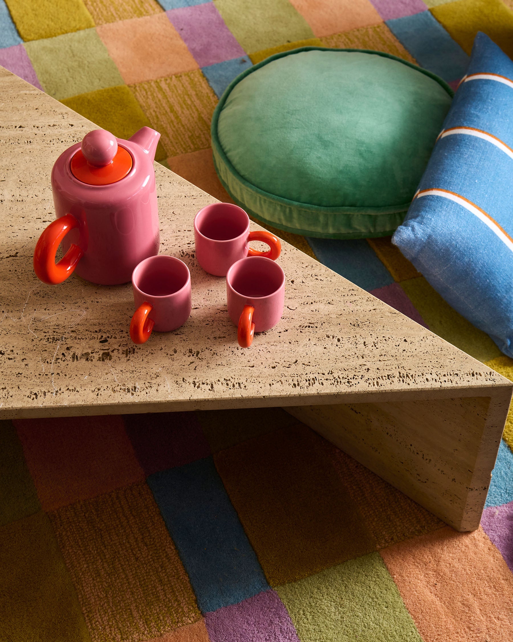Pink espresso mugs with teapot displayed on wooden table with colorful striped cushions