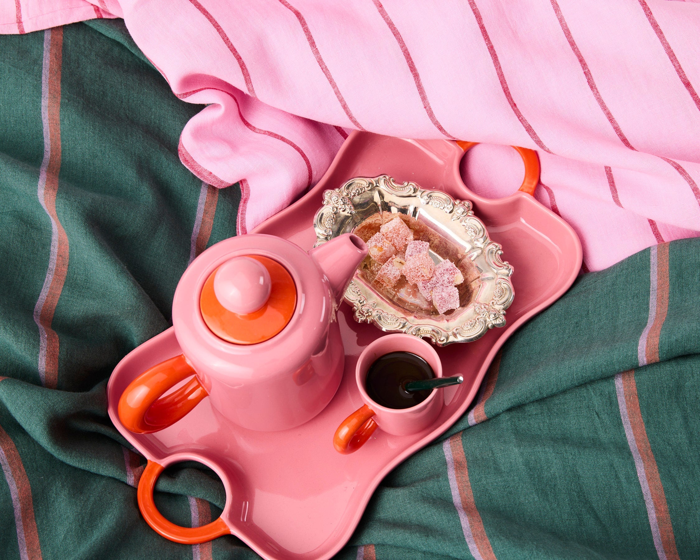 Pink espresso teapot and mug with orange handles on decorative tray with Turkish delight