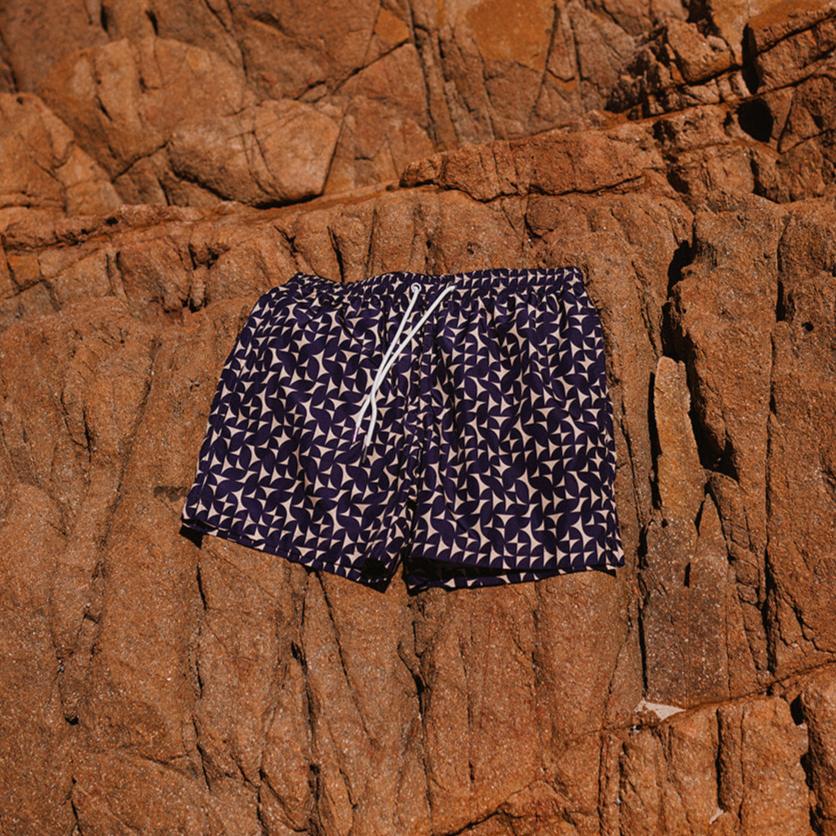 Navy blue swim shorts with white pattern on a rocky surface