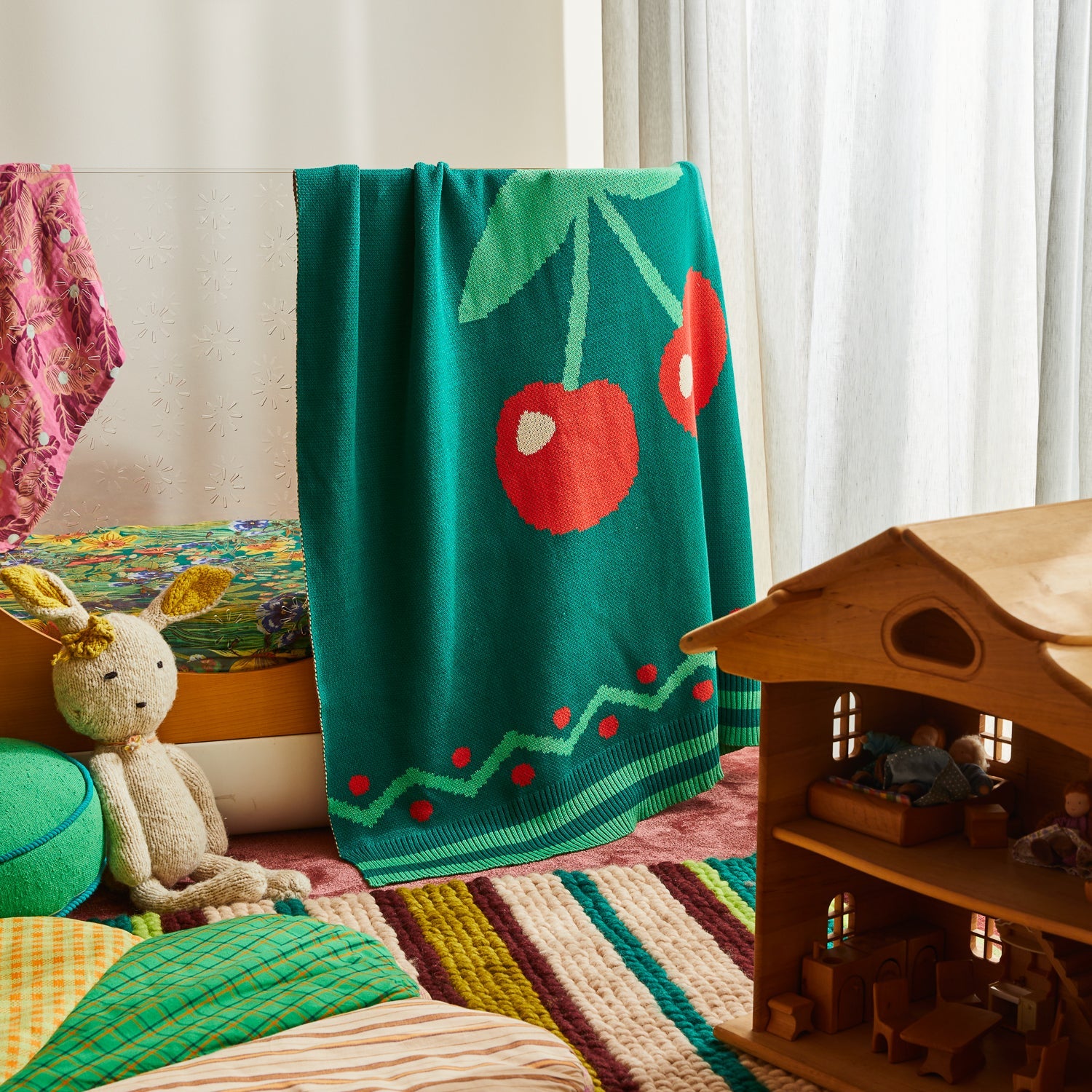 Tea Baby Blanket in green knit with red cherry pattern displayed in colorful nursery playroom