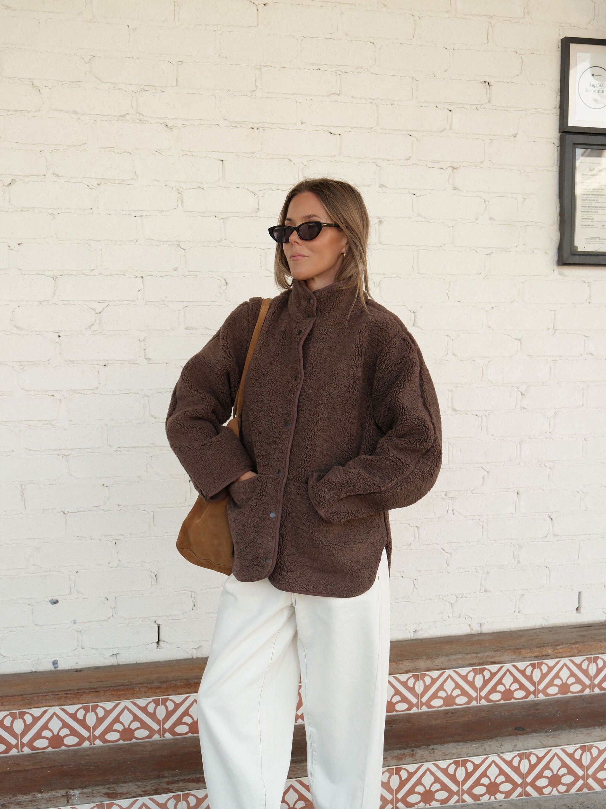 Three quarter view of chocolate brown teddy jacket styled with white pants showing relaxed silhouette