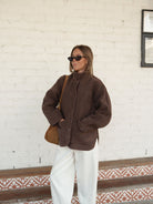 Three quarter view of chocolate brown teddy jacket styled with white pants showing relaxed silhouette