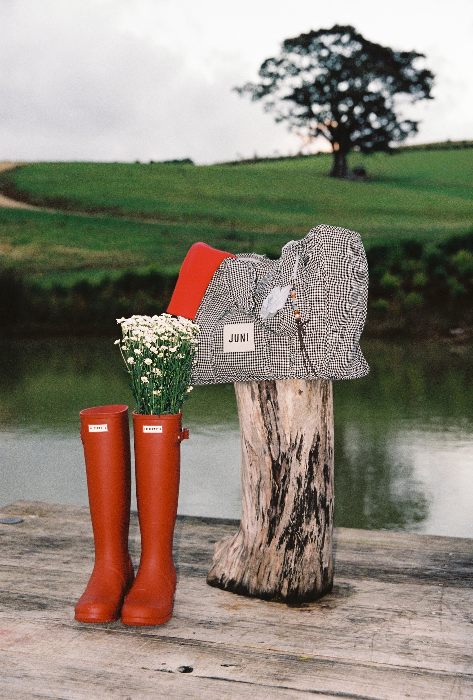 Vichy gingham Everything Bag styled outdoors on wooden post beside red boots and wildflowers