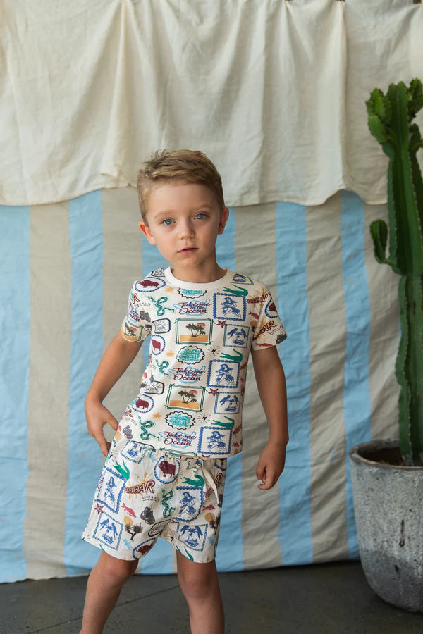 boy wearing The adventure-inspired tiled print t-shirt features crocodiles, snakes, boxing gloves, palm trees, parrots, and the phrase “Take me to the ocean” — sparking imagination while adding a vibrant, playful edge to your child’s wardrobe.