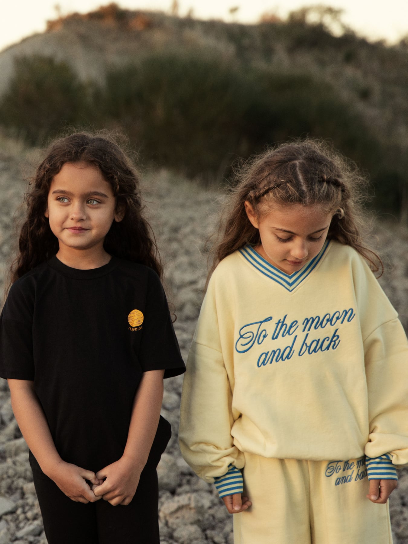 Two children wearing mini rodini To the Moon collection in outdoor natural setting