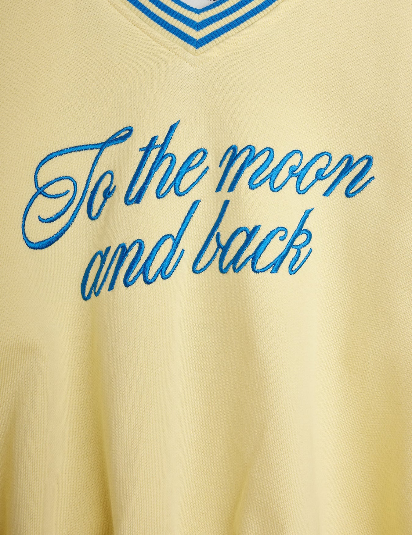 Close-up detail of blue embroidered To the Moon and back script lettering on yellow fabric