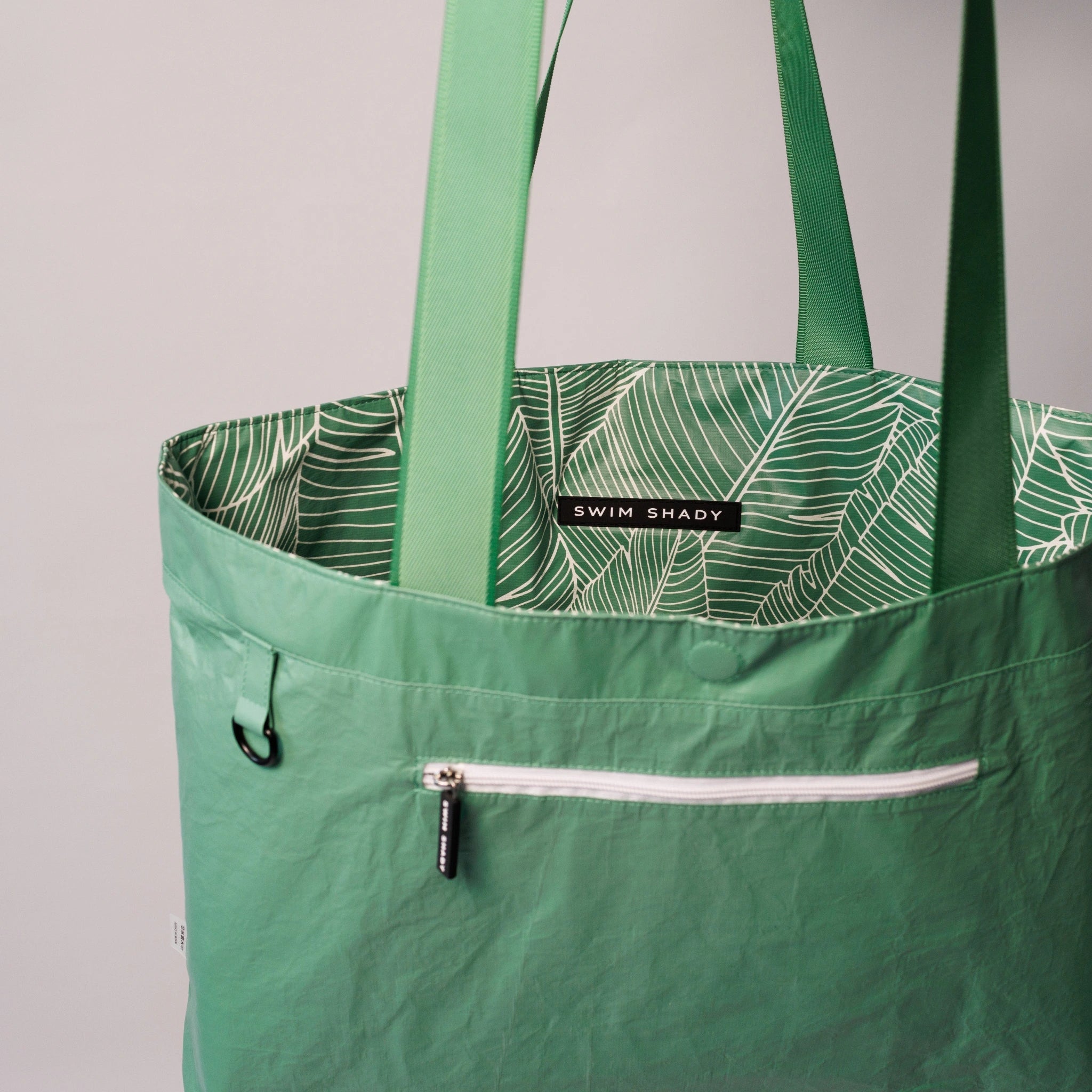 Green tote bag with leaf pattern interior and 'Swim Shady' label on a gray background
