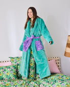 Woman standing on bed wearing teal Tropicas Cosy Robe with purple belt showing long sleeve style