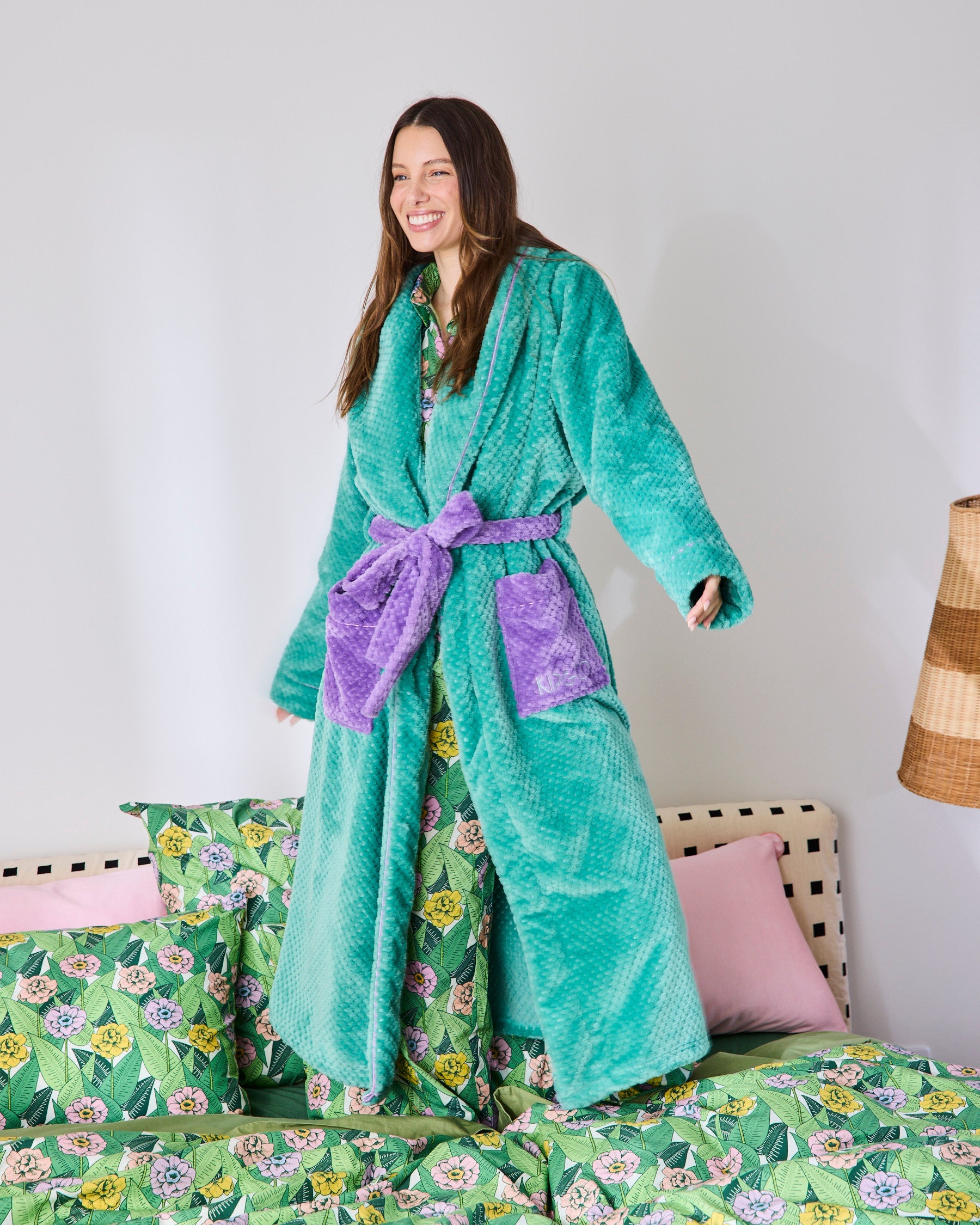 Woman standing on bed wearing teal Tropicas Cosy Robe with purple belt showing long sleeve style