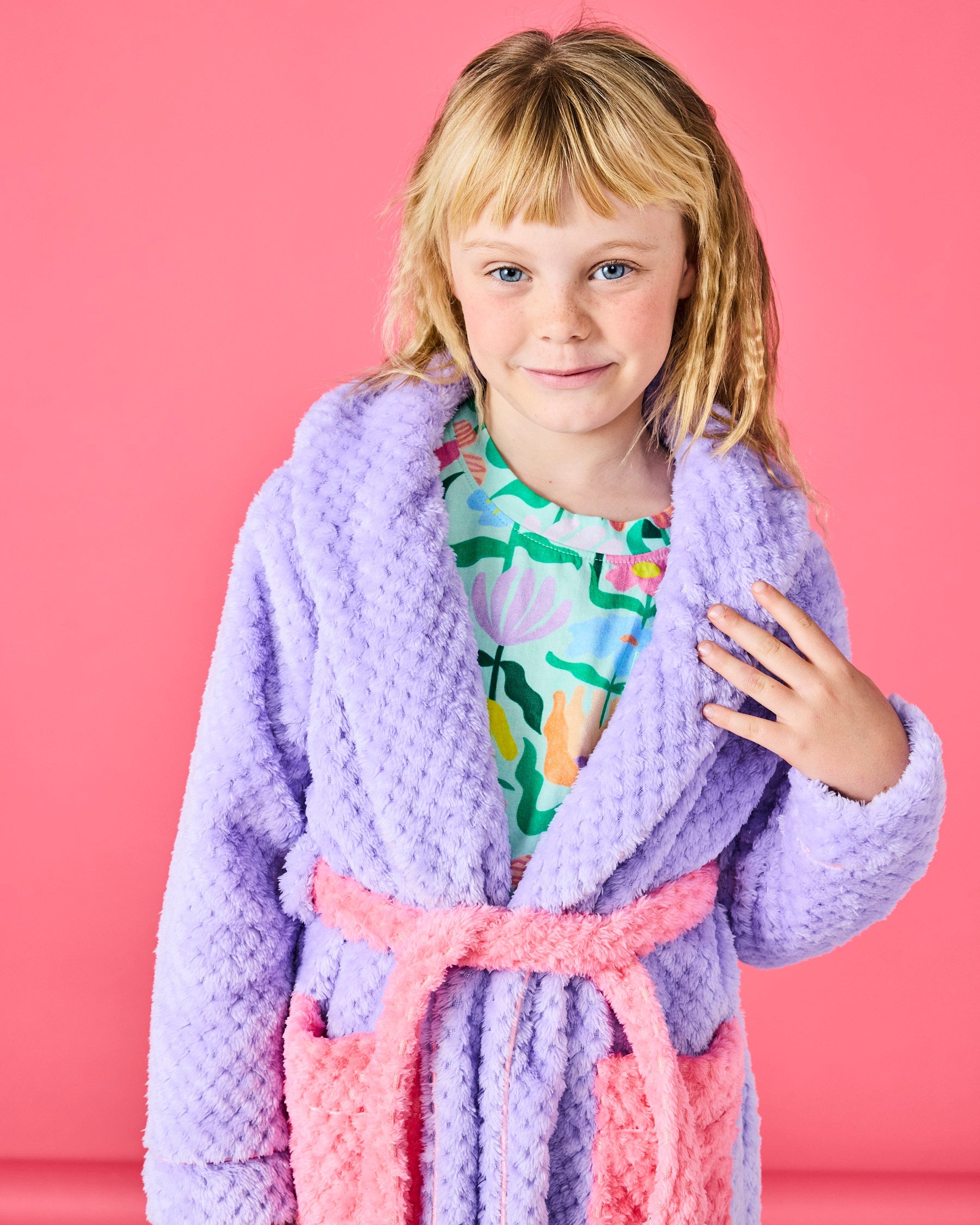 Front view of Tulip Kids Cozy Robe in purple with pink trim worn by child on pink background