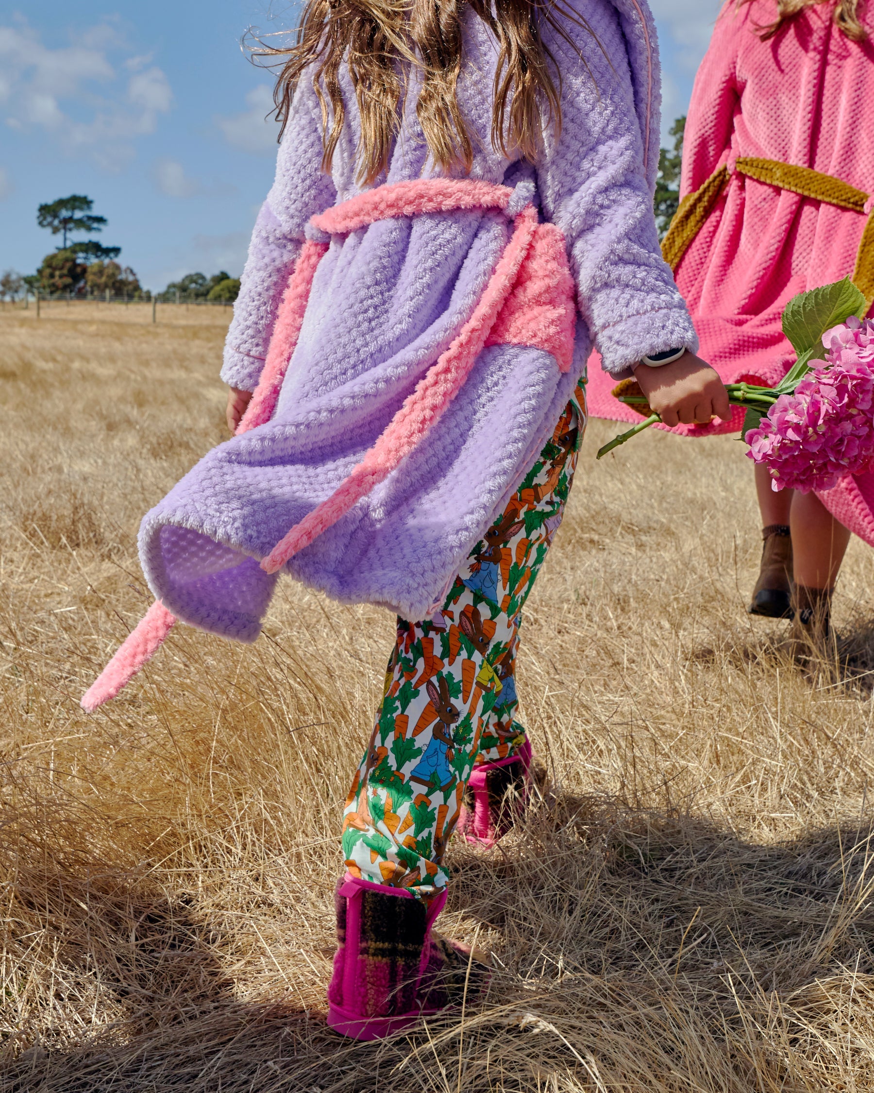 Child wearing purple Tulip Kids Cozy Robe with pink trim walking through golden field outdoors