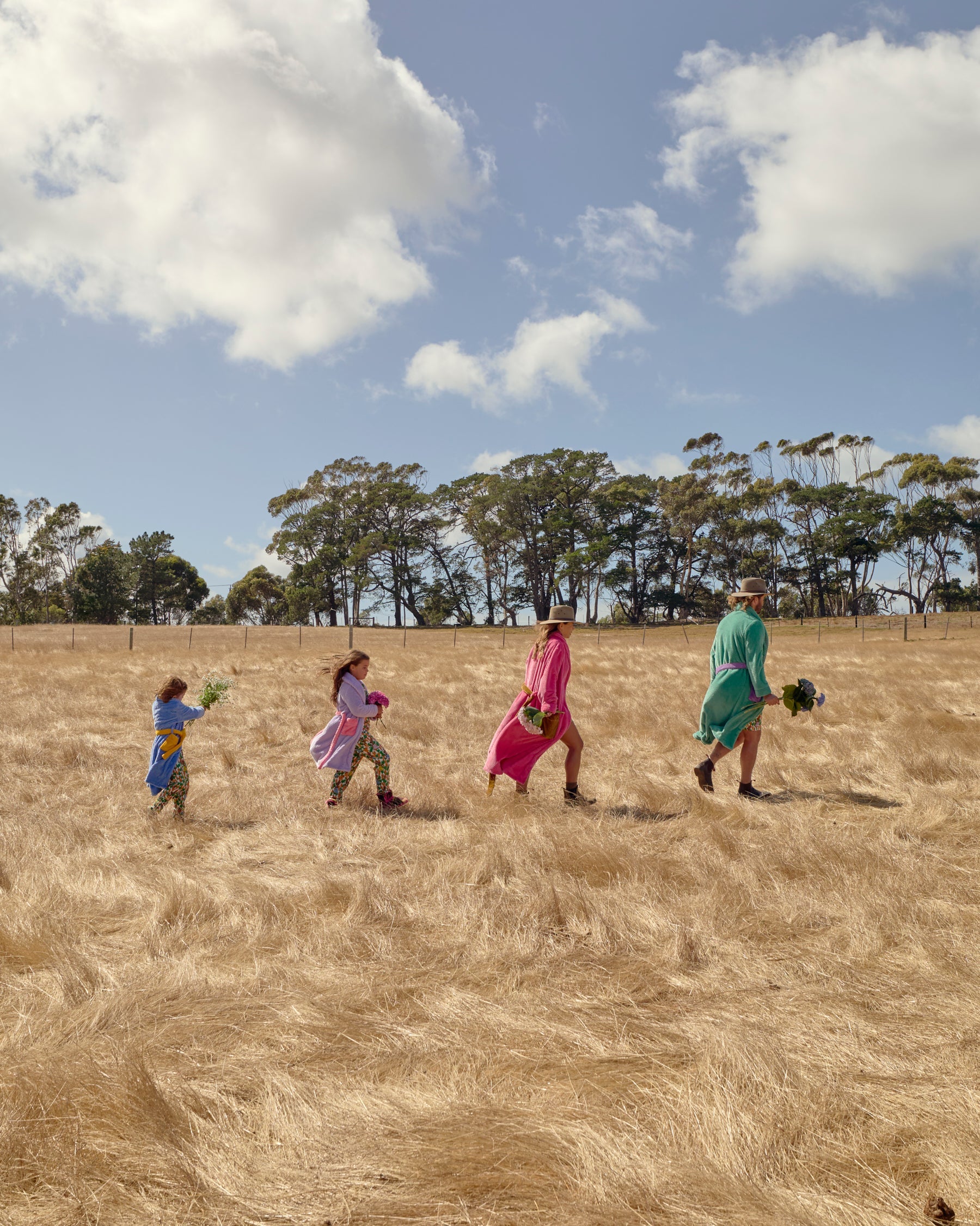 Wide outdoor shot of family in colorful Kip & Co robes walking through golden field