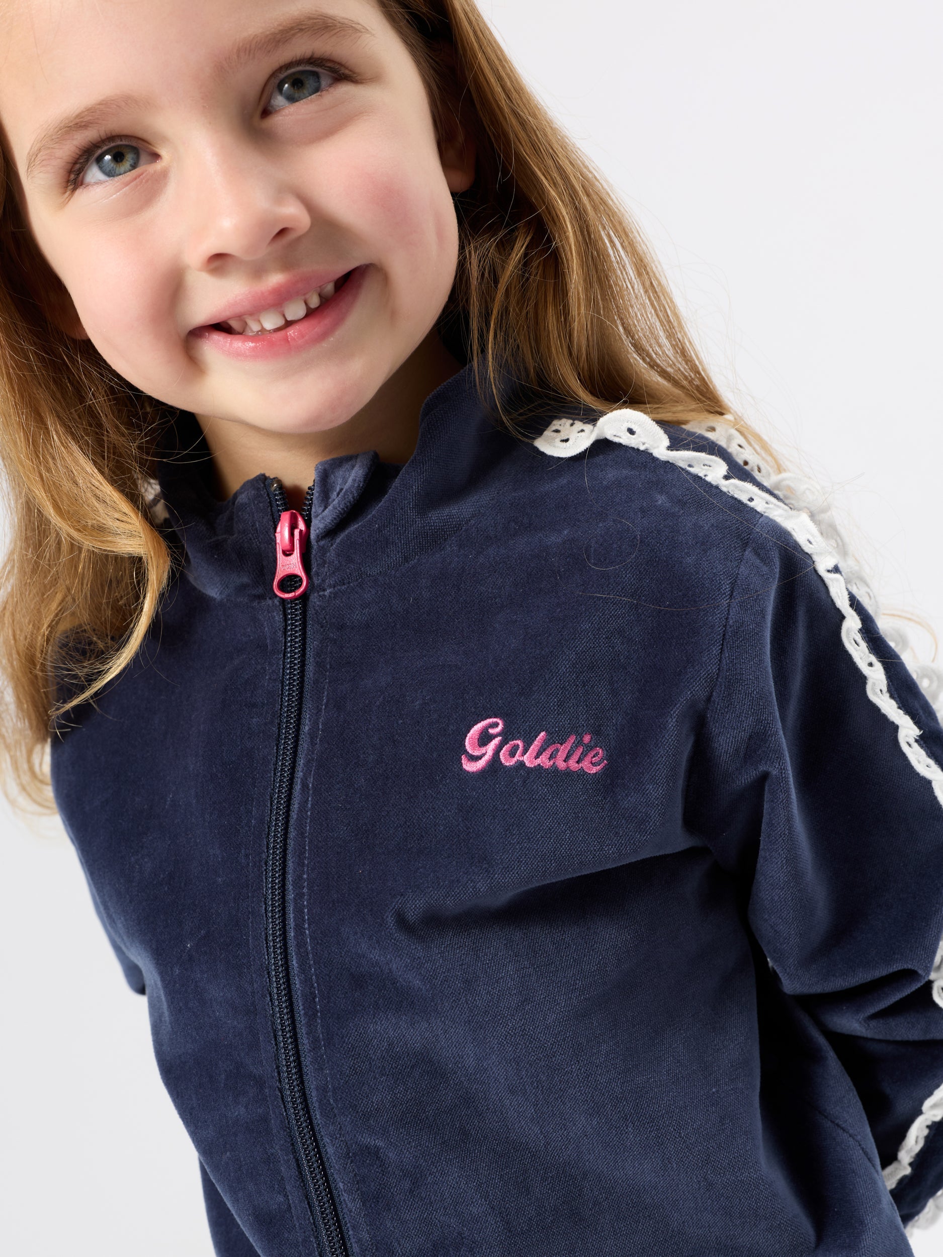 Close-up detail of navy velour sweat jacket showing pink embroidered script logo and white broderie shoulder trim
