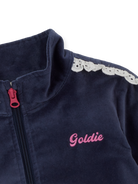 Detail shot of navy velour jacket showing pink zipper pull and white broderie lace trim on shoulder