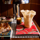 Pearl Violetta Vase with ruffled rim styled on a tiled shelf beside a lit candle and coffee table books
