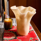 Pearl Violetta Vase with ruffled rim shot up close on a floral-patterned surface beside a glowing candle