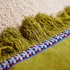 Close-up of juniper green fringe trim and decorative woven tape edge detail on applique cushion