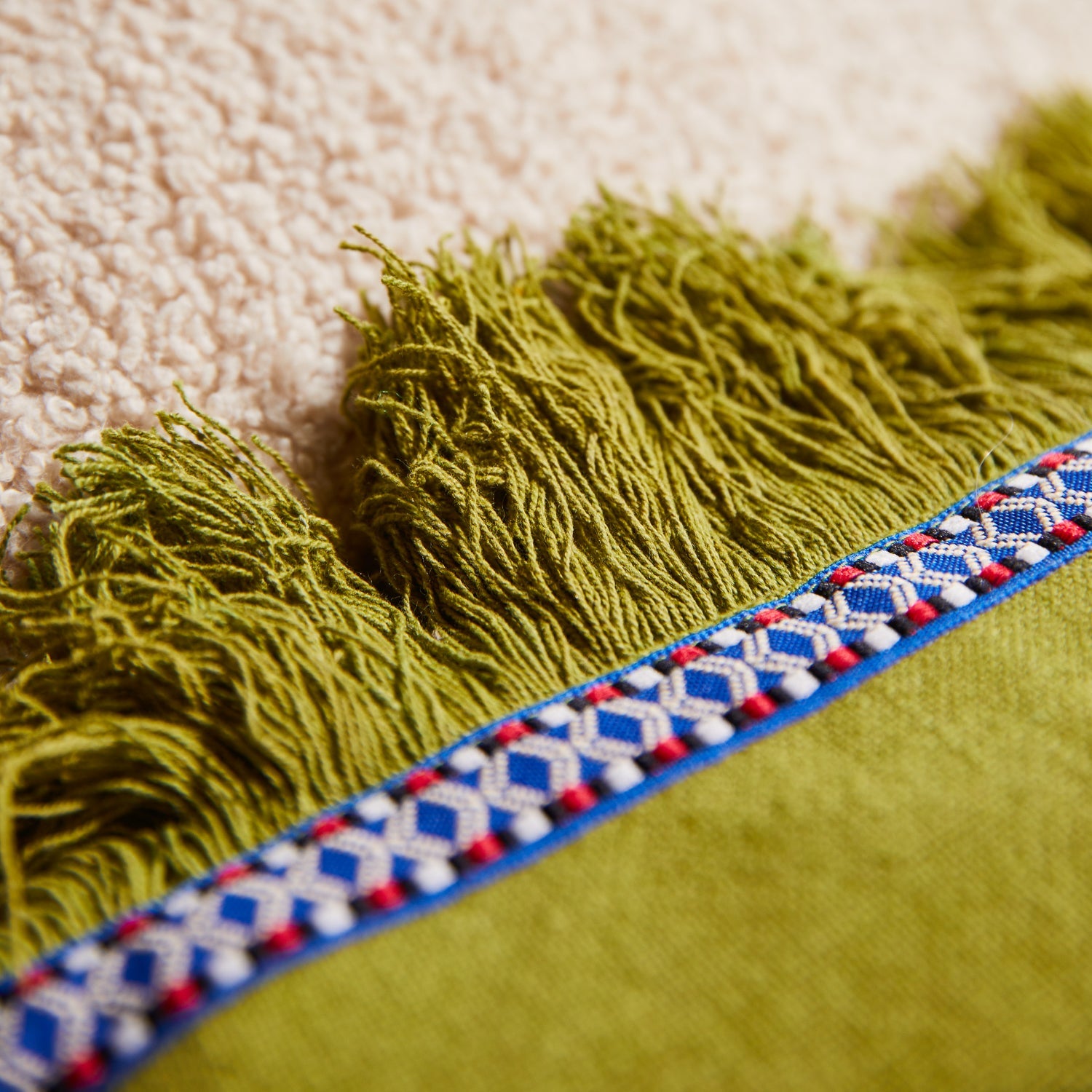 Close-up of juniper green fringe trim and decorative woven tape edge detail on applique cushion