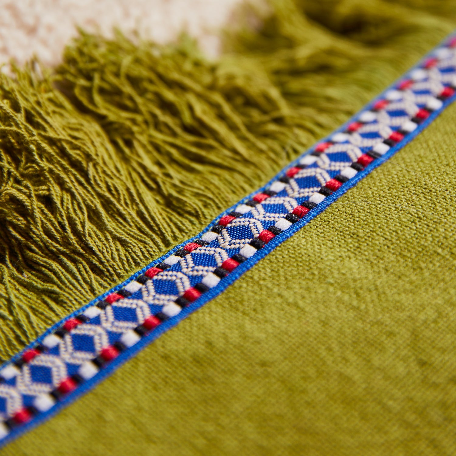 Detail shot showing juniper green fringe edge and blue red white geometric tape trim on cushion
