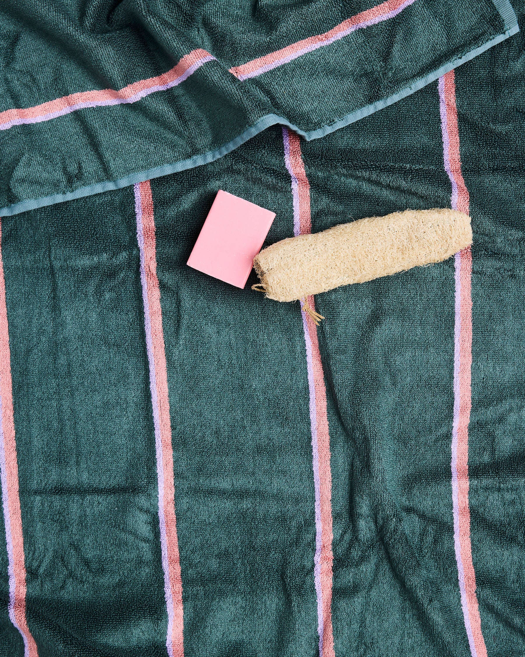 Close-up of green bamboo terry bath sheet with pink stripe pattern and soap styling props