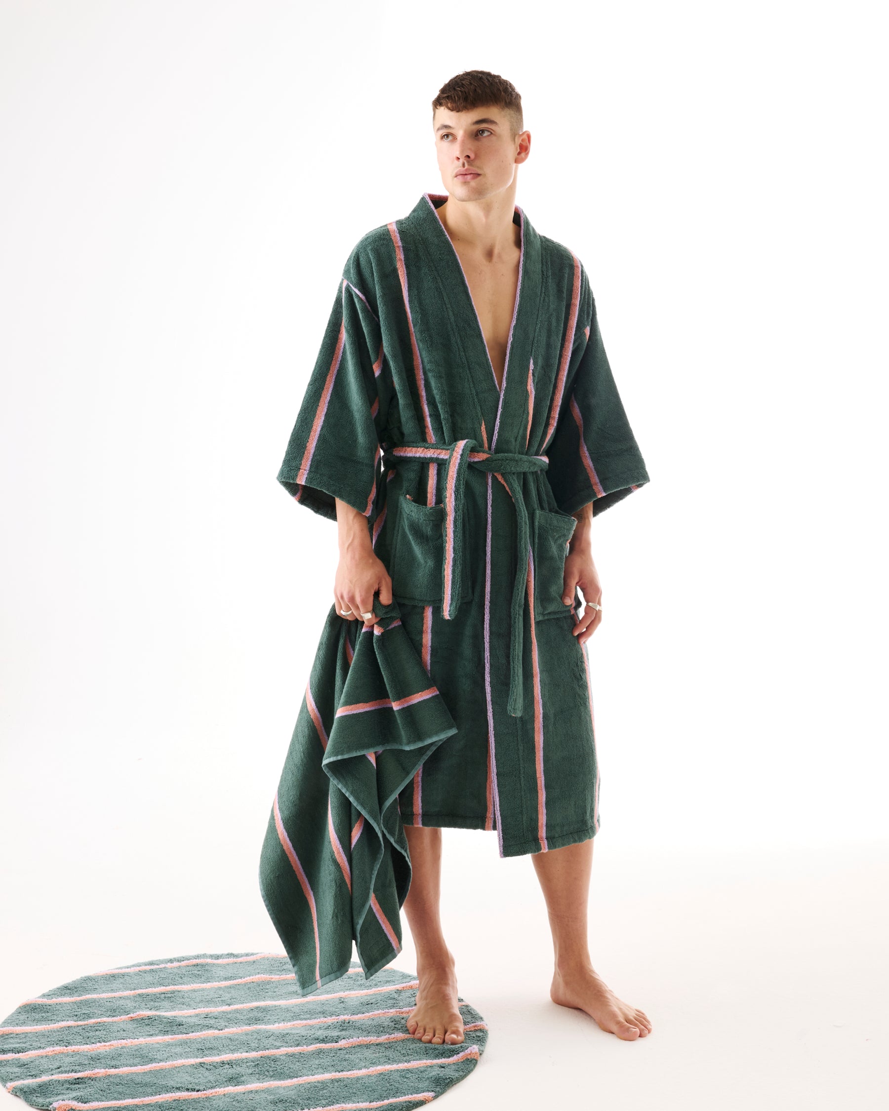 Male model wearing green striped bamboo terry bath robe with matching bath sheet on floor
