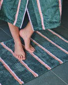 Person stepping onto Wakame Crush Stripe Bath Mat showing green base with pink coral striped pattern