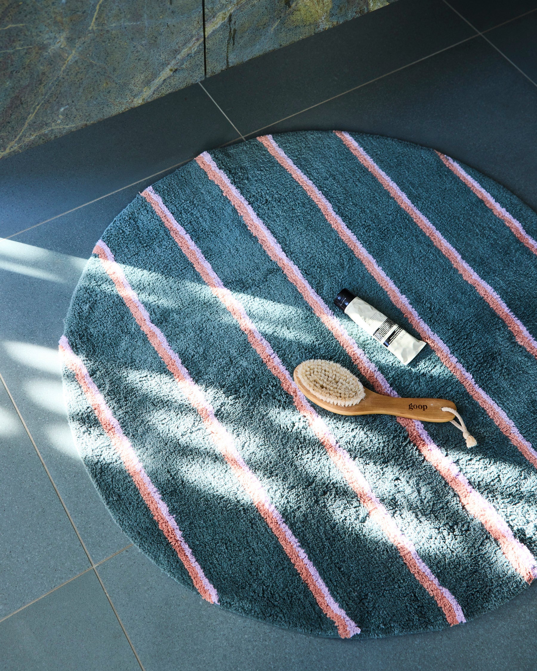 Overhead view of Wakame Crush Stripe Round Bath Mat by Kip & Co with teal and pink striped pattern on bathroom floor