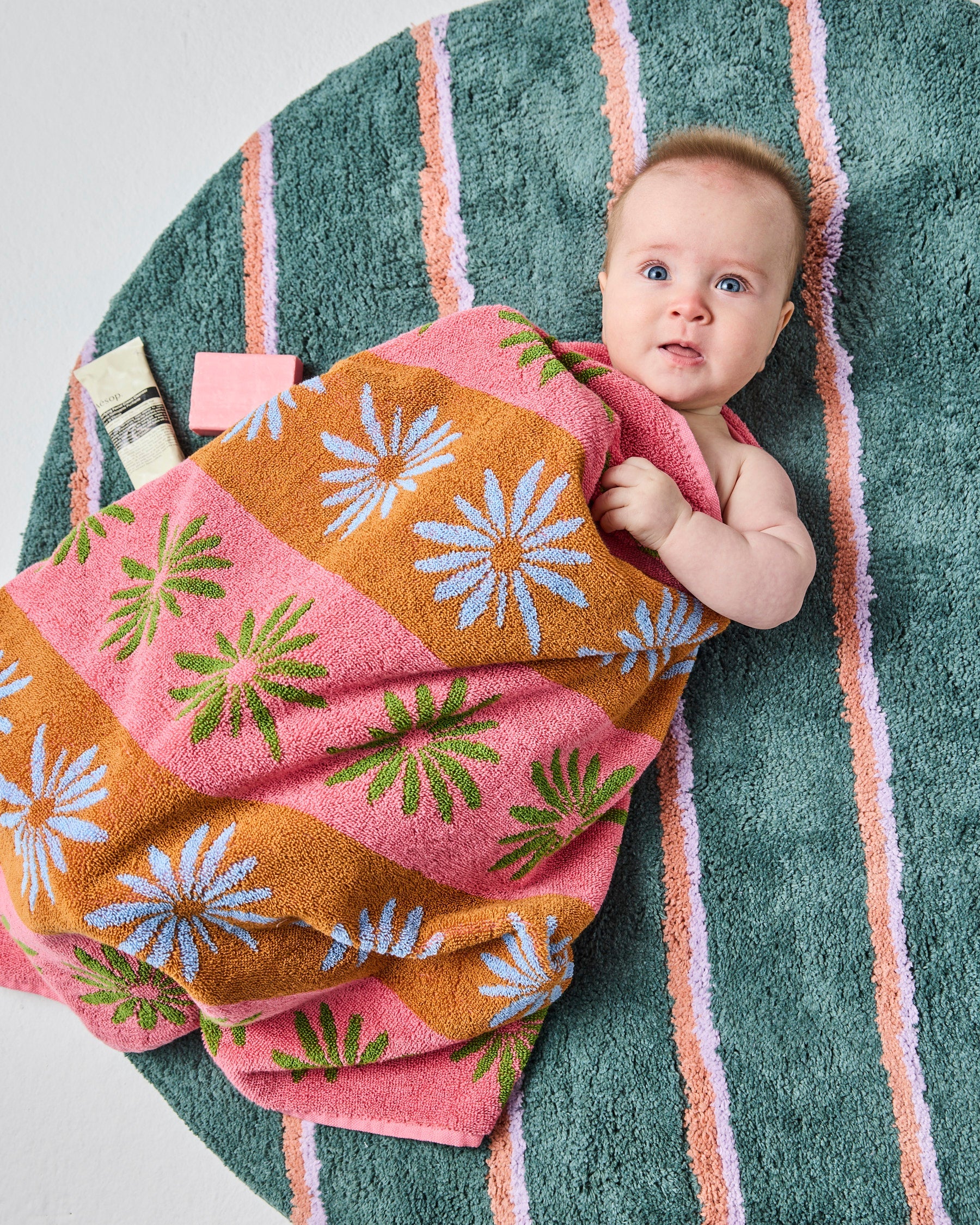 Close-up lifestyle shot showing baby on Wakame Crush Stripe Round Bath Mat highlighting soft tufted texture and colors