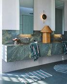 Partial view of Wakame Crush Stripe Round Bath Mat on bathroom floor beneath marble vanity with matching towels