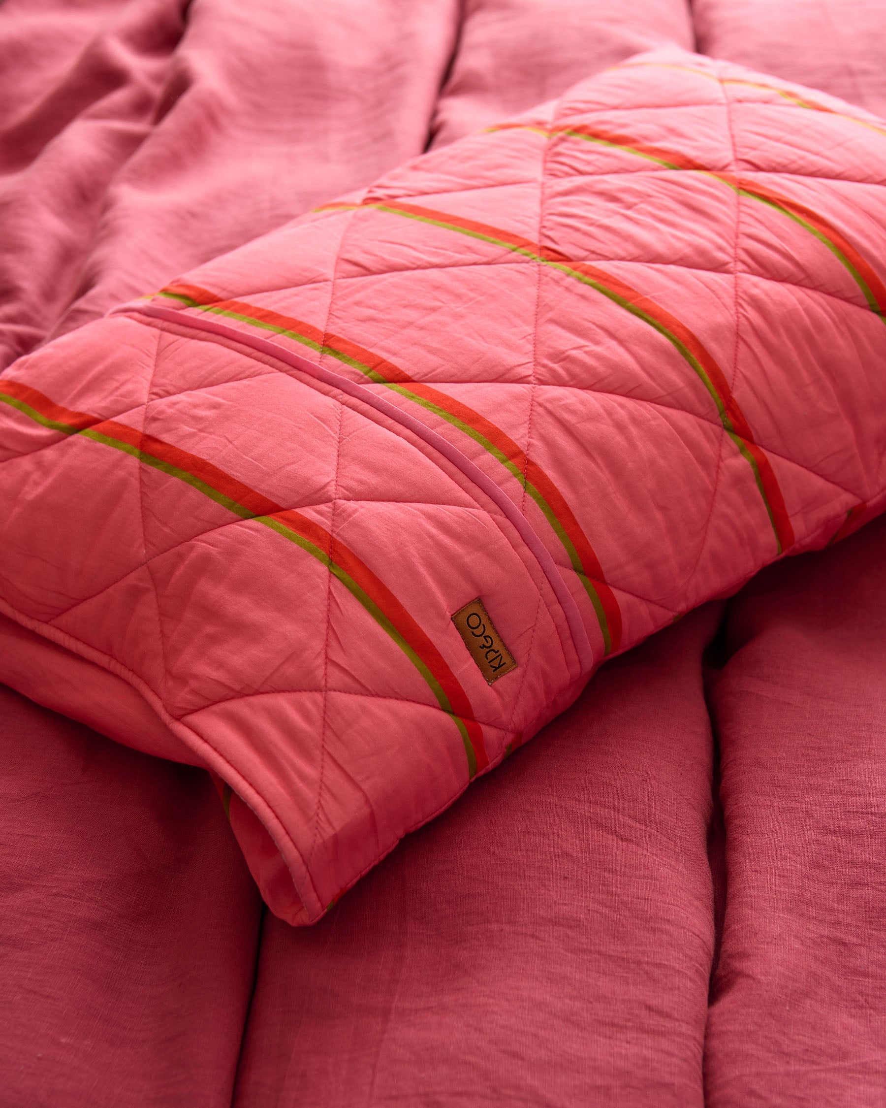 Single Kip Co Wategos Soiree quilted pillowcase on coral sofa showing quilted texture and brand label