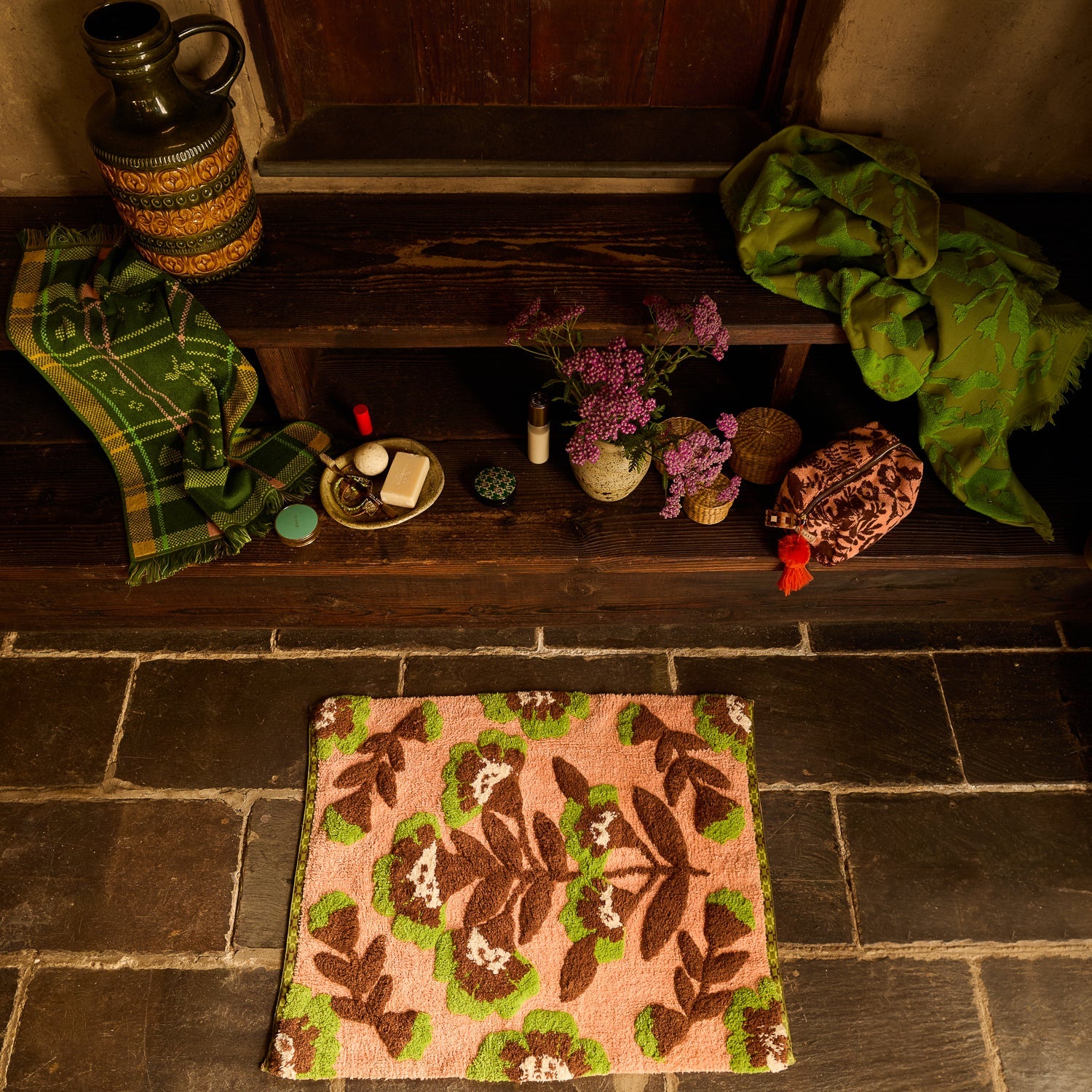 Carnelian Winona Bath Mat on dark stone floor, overhead angle showing pink base with brown and green leaf tufted design