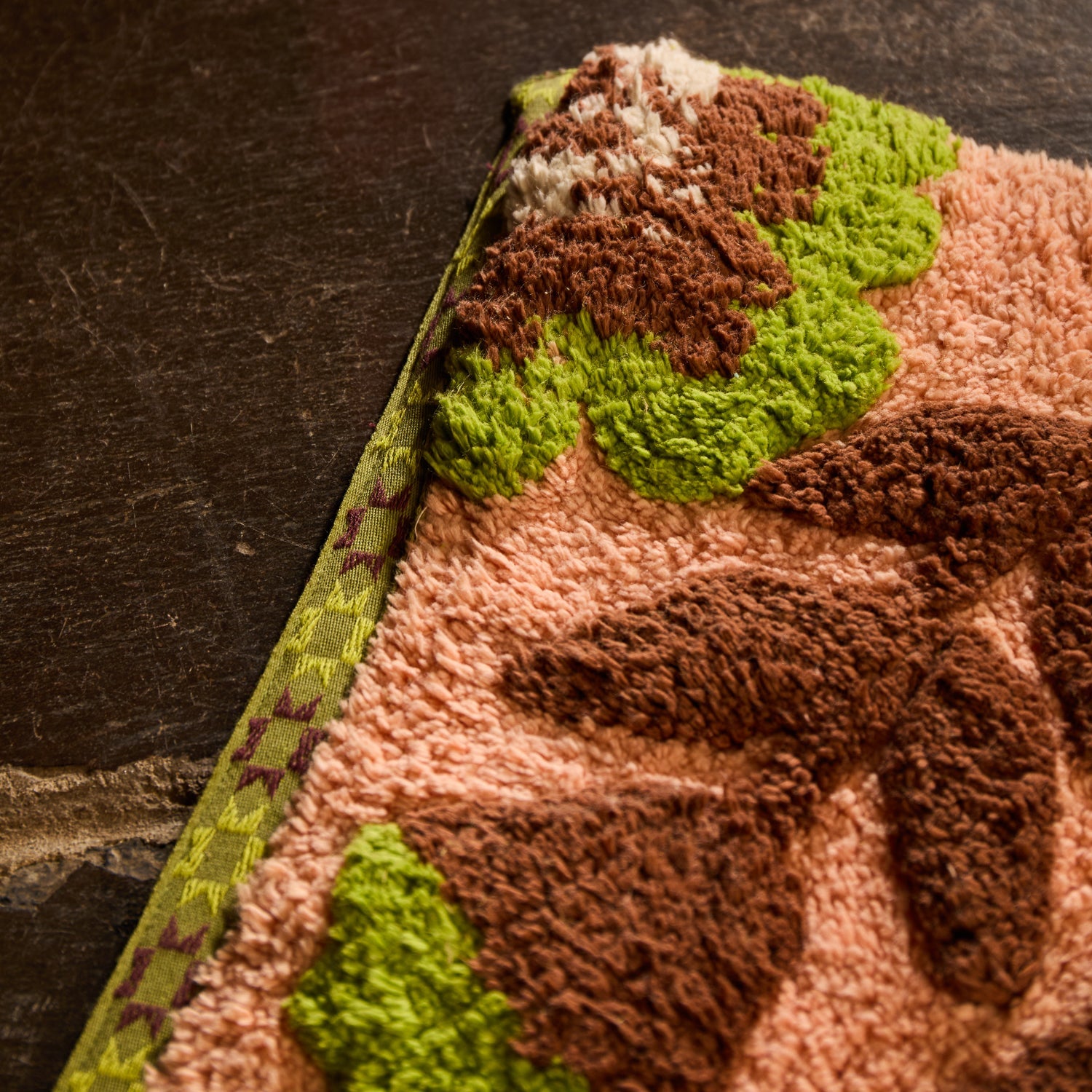 Close-up corner detail of the Carnelian Winona Bath Mat showing tufted texture and woven green border edge
