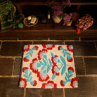 Moonlight Winona Bath Mat with red floral and teal leaf pattern placed on a stone floor below a wooden shelf