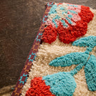 Close-up corner detail of the Moonlight Winona Bath Mat showing tufted red floral, teal leaves and woven border trim