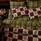 Brown and white checkerboard floral and bird print cotton pillowcase set styled on a bed with green tartan bedding, overhead view