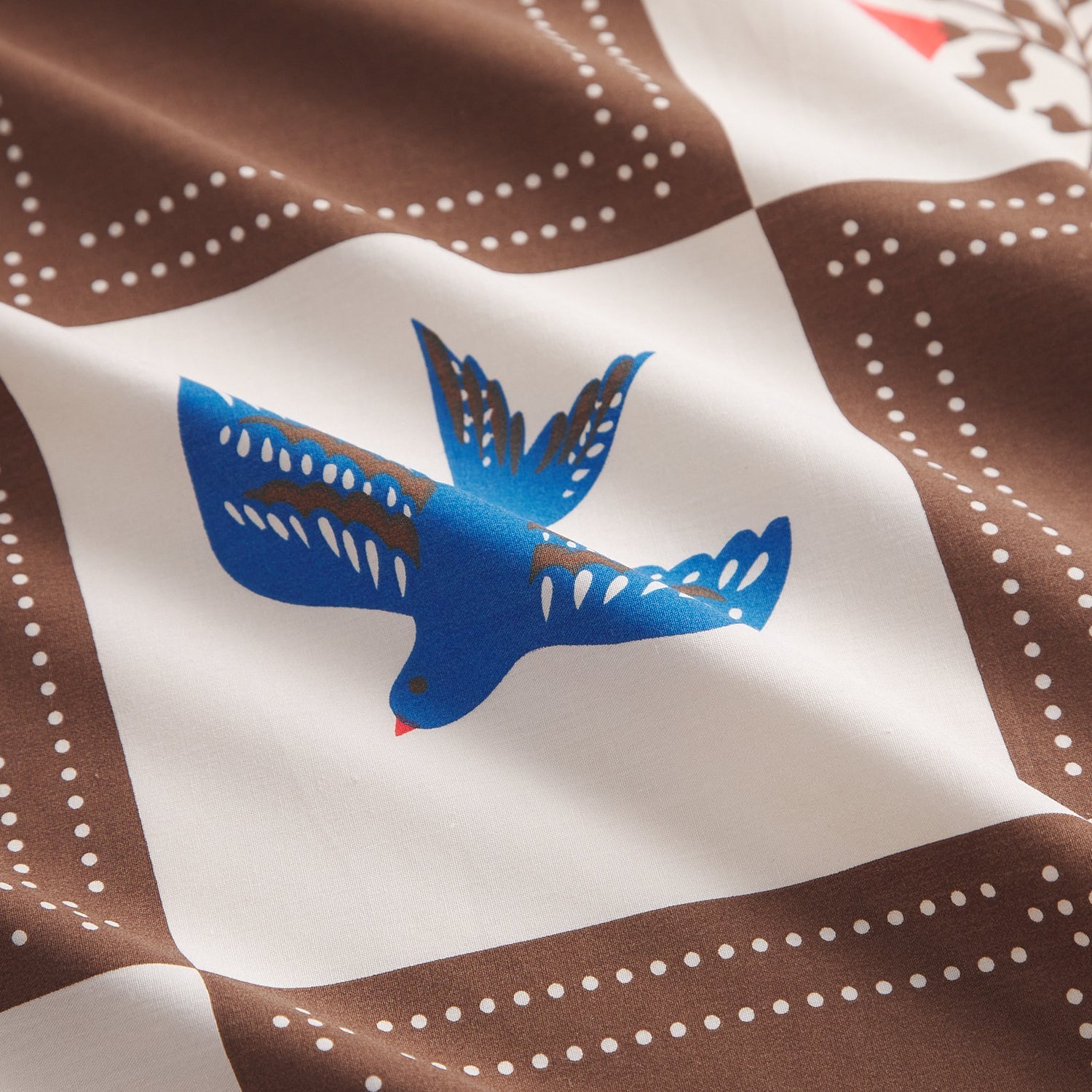 Close-up detail of blue bird motif on brown and white checkerboard cotton pillowcase fabric