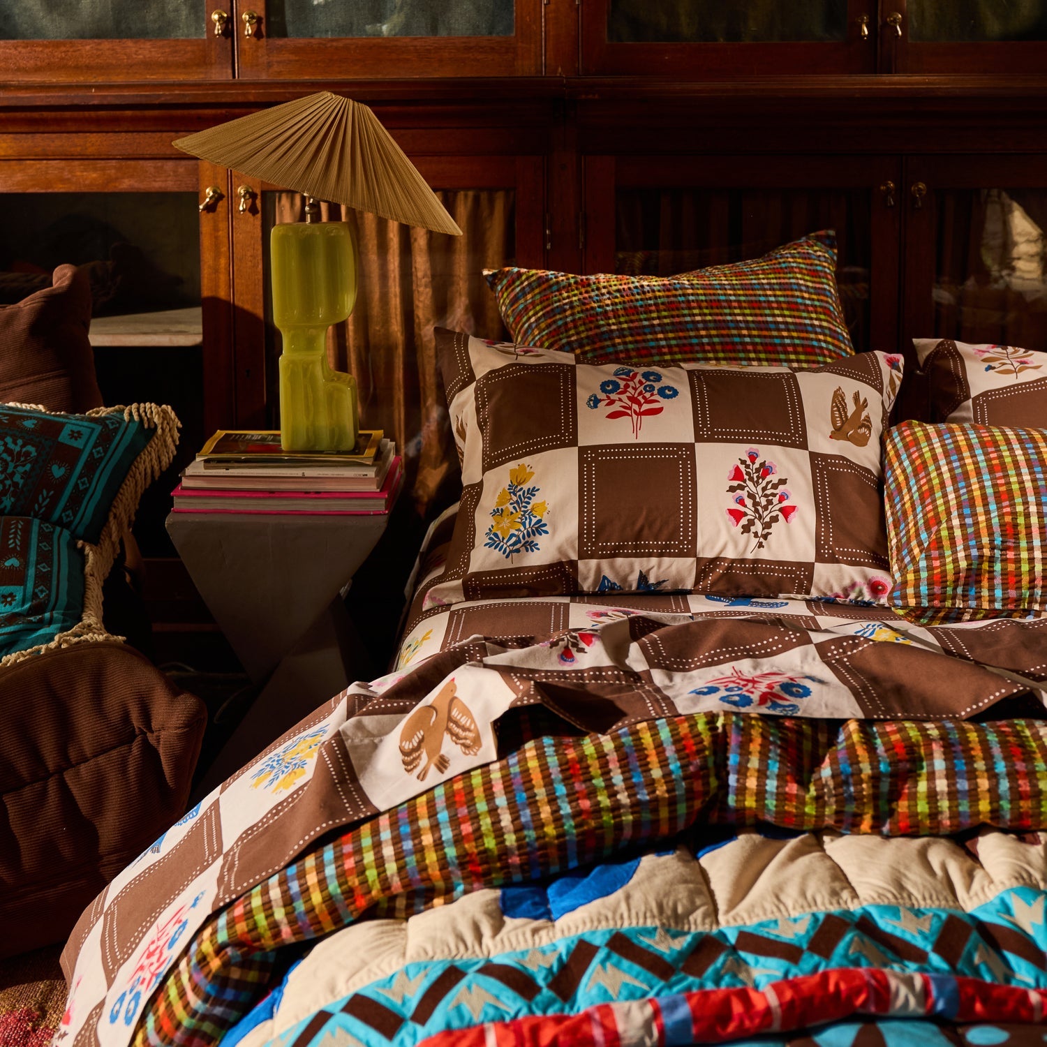 Brown and white checkerboard floral and bird print cotton pillowcase styled on a layered bed in a dark wood bedroom