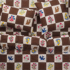 Close overhead view of brown and cream checkerboard quilt cover with matching pillowcases showing bird and floral print