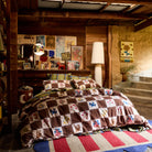 Wide shot of brown and cream checkerboard cotton quilt cover with bird and floral print on a bed in a rustic cabin room