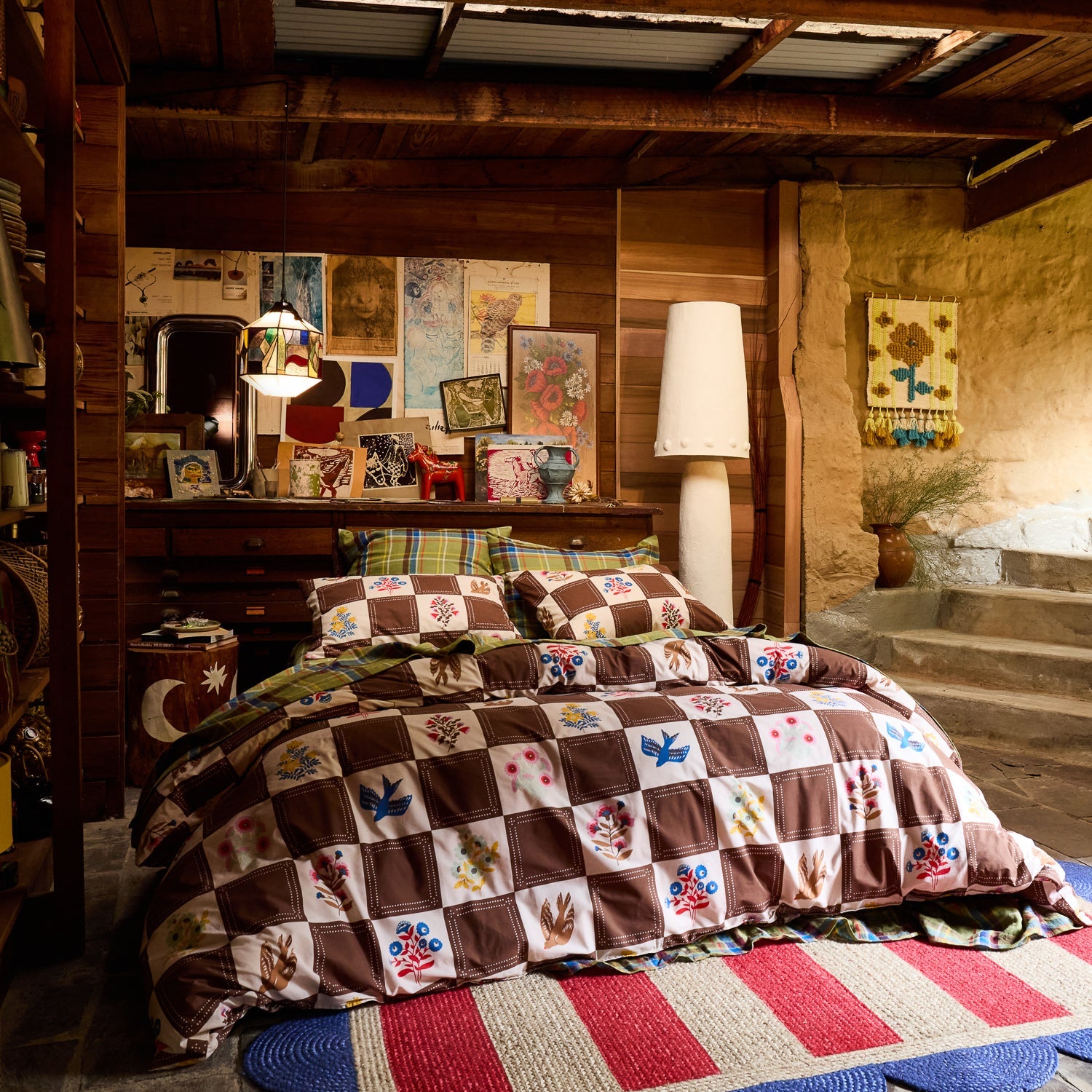 Wide shot of brown and cream checkerboard cotton quilt cover with bird and floral print on a bed in a rustic cabin room