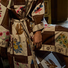 Close-up of cotton robe showing brown and cream checkered print with bird and floral motifs, tie belt and patch pocket detail